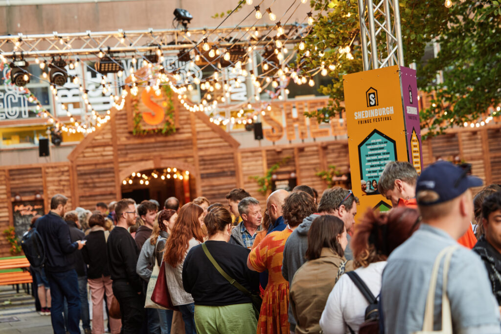 A group of people queue for a show outside of Shedinburgh.
